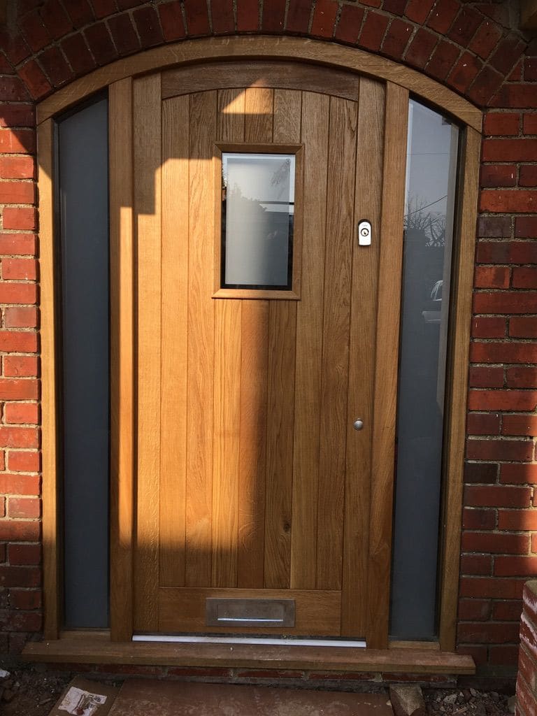 Arched oak front door with glazed side panels in a brick opening