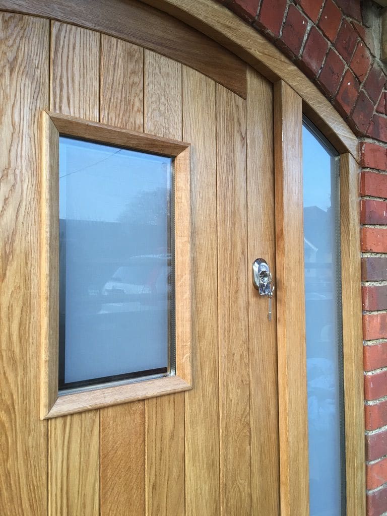 Close detail of an oak front door with a glazed panel and arched frame