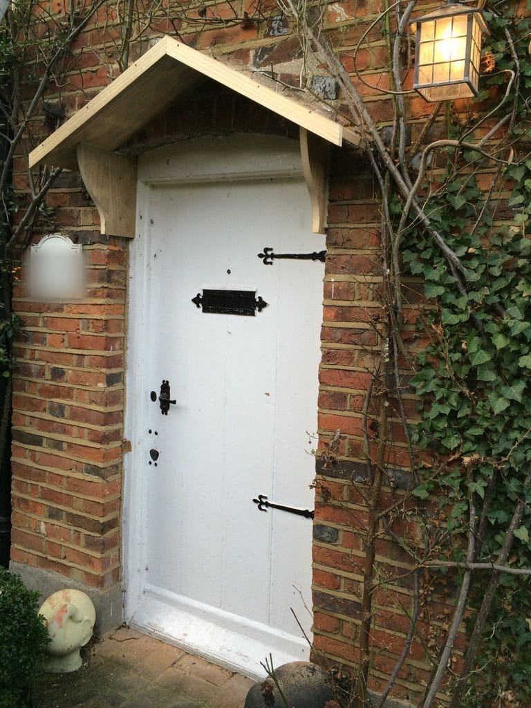Painted ledged cottage door with black strap hinges under a timber canopy