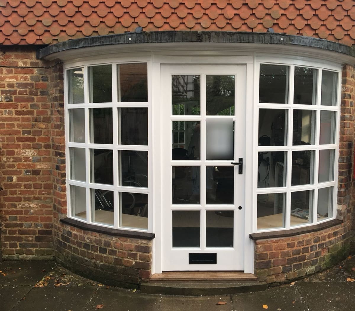 Curved timber bow window and glazed door set into an old brick shopfront
