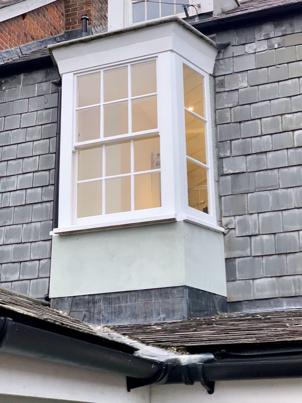 Six-over-six timber sash window in an oriel bay on a slate-hung wall