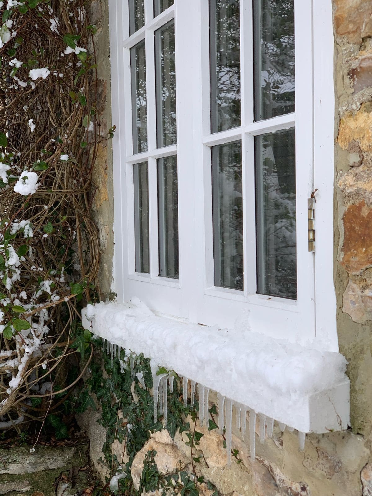 Snow and icicles along the deep sill of a white painted timber casement window