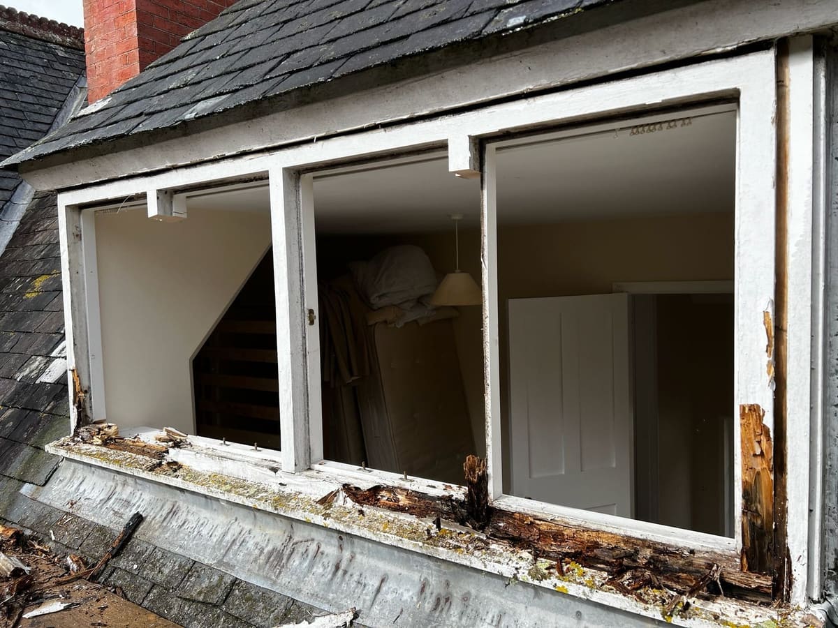 Rotten timber dormer window frames on a slate roof before replacement