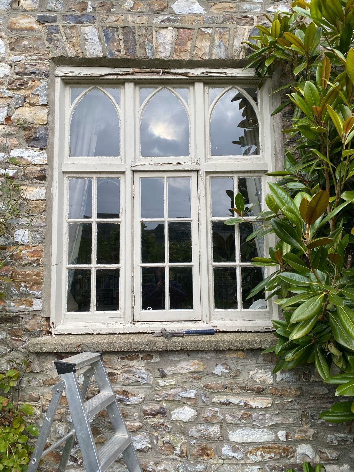 Weathered painted casement window with Gothic arched heads in a stone wall