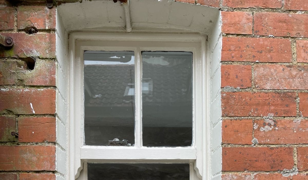Upper sash and horns of a painted timber sash window in a red brick wall