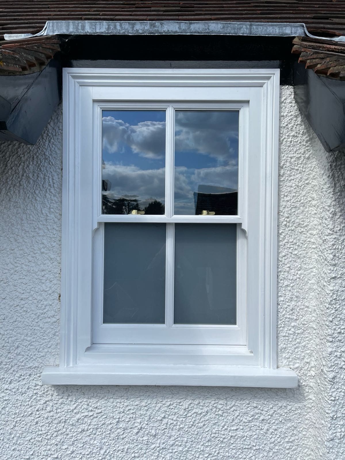 White painted timber sash window with glazing bars and horns in a rendered wall